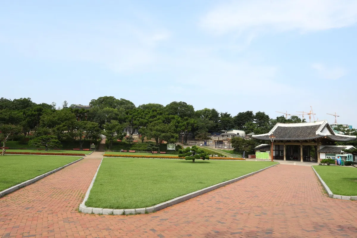 잔디밭 사이로 붉은 길이 나 있고 뒤쪽에 한옥 건물이 보이는 공원
