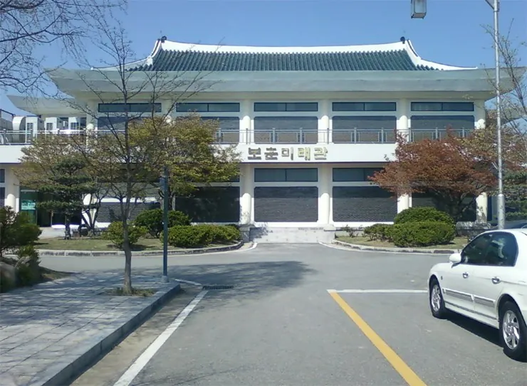 푸른 기와지붕을 얹은 넓은 건물 앞 주차장 풍경
