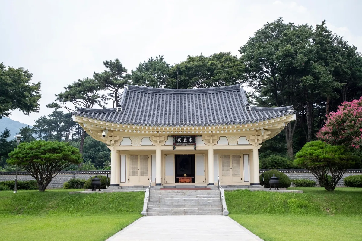 숲을 배경으로 돌계단 위에 선 기와지붕 사당 건물