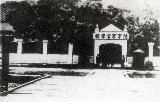 울타리 사이로 현판이 걸린 학교 정문이 보이는 흑백 사진