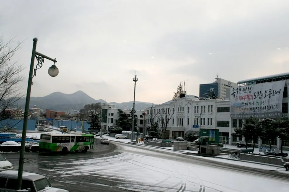 흐린 하늘 아래 넓은 광장 끝에 선 흰 관공서 건물