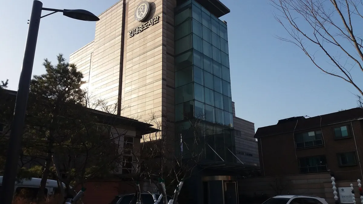 가로수 뒤로 보이는 유리 외벽의 여러 층짜리 건물