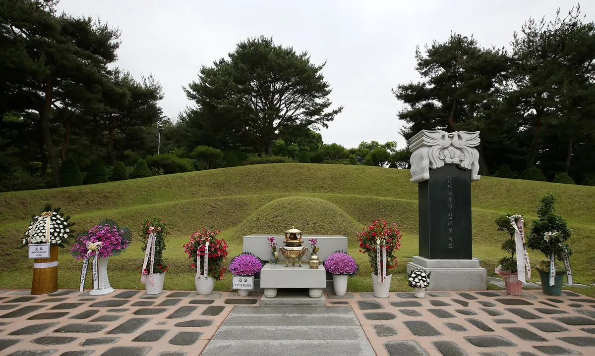 잔디 봉분 앞에 비석과 상석이 놓이고 꽃이 둘러진 묘역