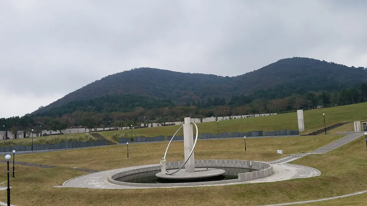 오름을 배경으로 넓은 잔디밭 가운데 둥근 추모 조형물이 놓인 모습